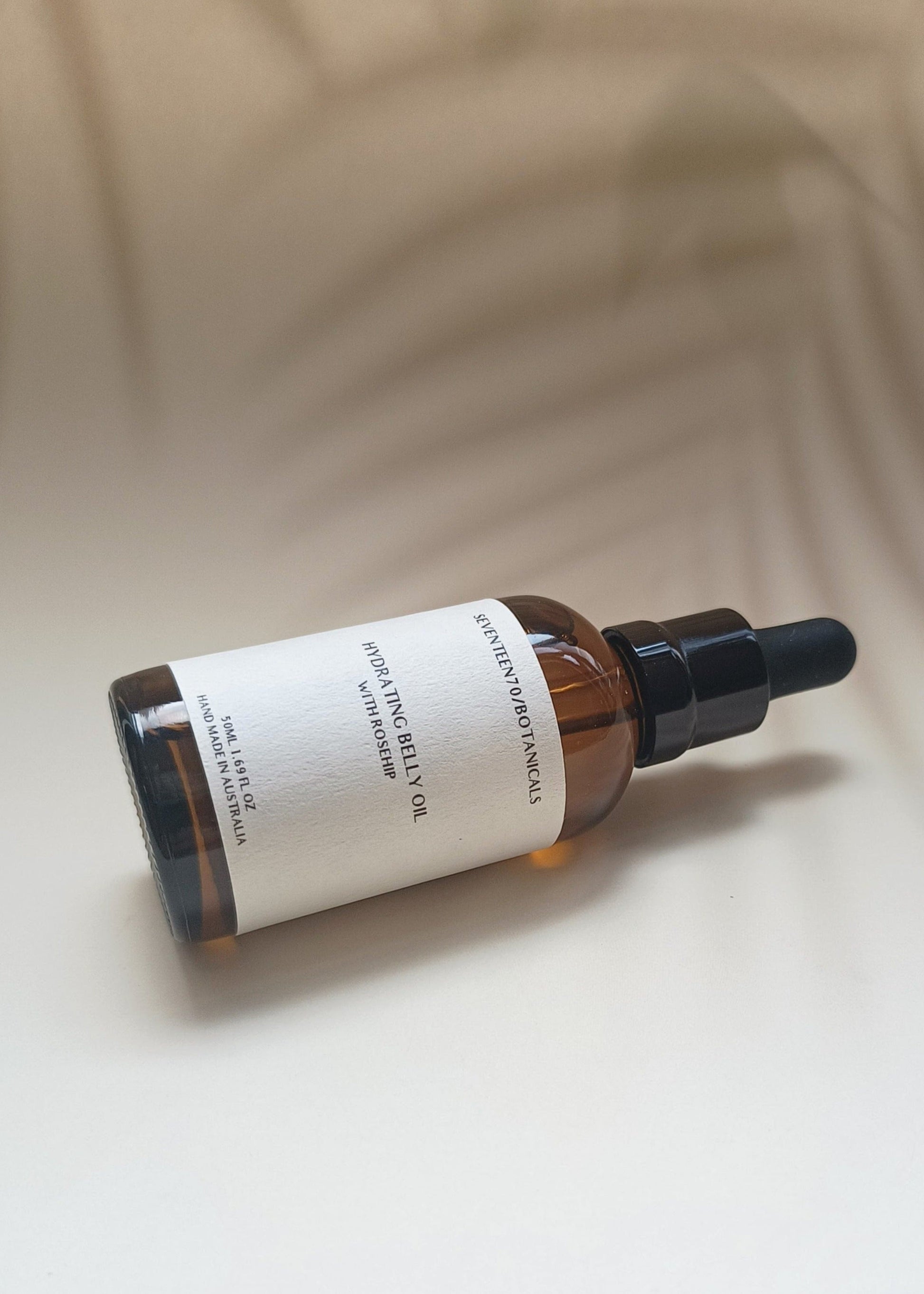 A bottle of Hydrating Belly Oil with Rosehip, displaying a clear amber liquid in a dark glass bottle with a black dropper. The label is white with text.