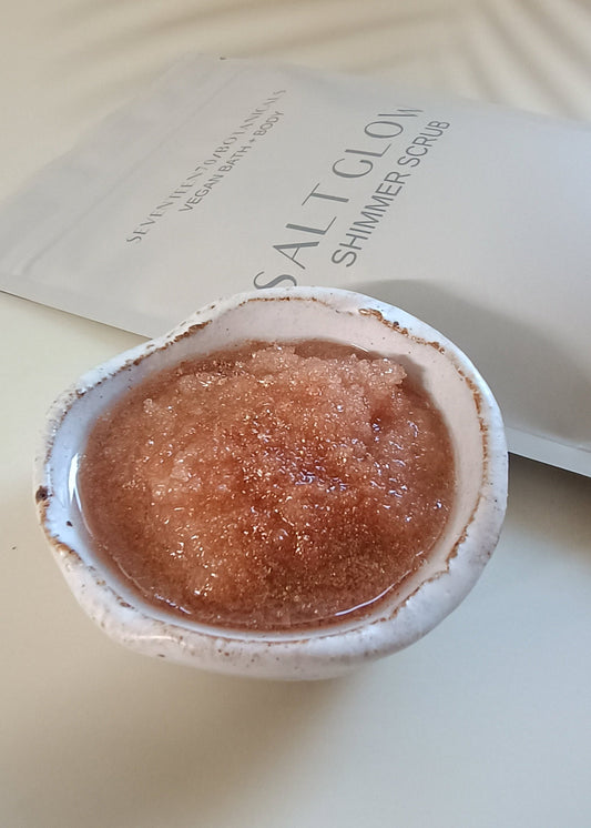 A pouch of Salt Glow Shimmer Scrub with a small container filled with the pinkish scrub powder beside it.