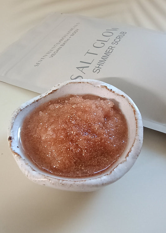 A pouch of Salt Glow Shimmer Scrub with a small container filled with the pinkish scrub powder beside it.