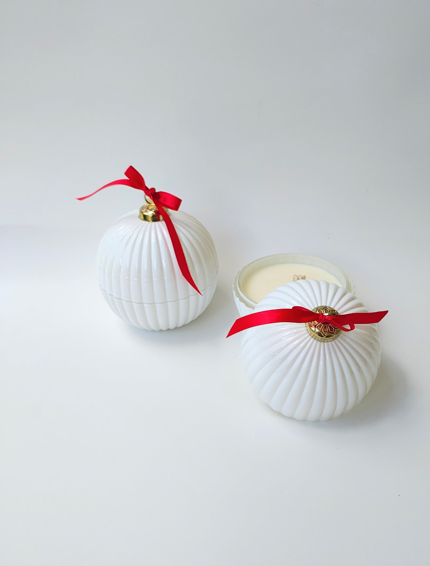 Two white shell-shaped containers with red ribbons and gold accents on a light gray background